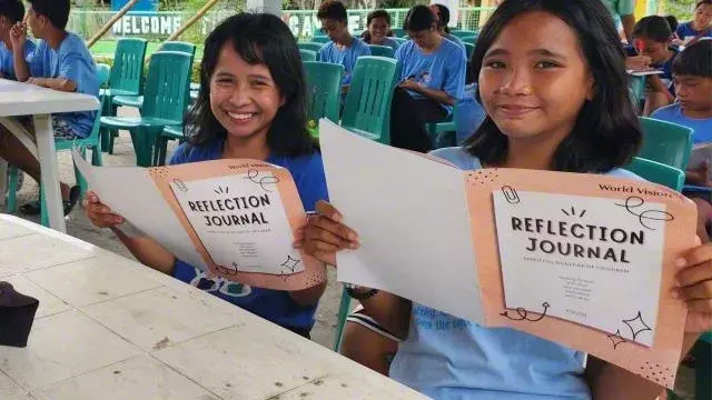 children holding out the reflection journal in Antique Philippines