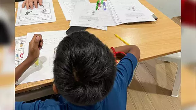A student writing in a workbook at a desk.