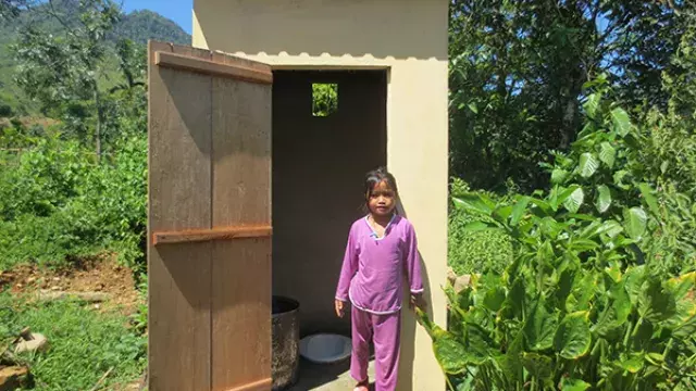 Child outside small concrete washroom in rural area