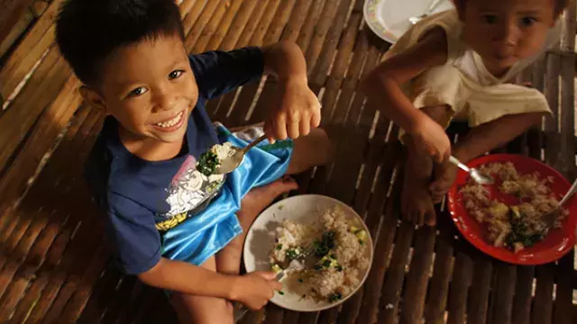 Two children eating rice and vegetables on bamboo floor