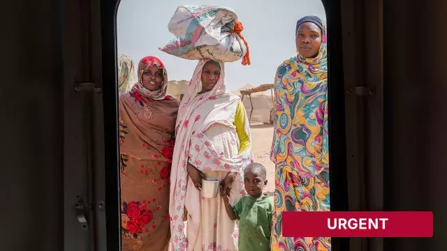 Adults and child in camp with urgent banner