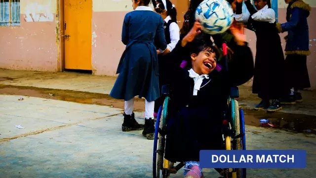 Child in wheelchair reaching for ball with dollar match label